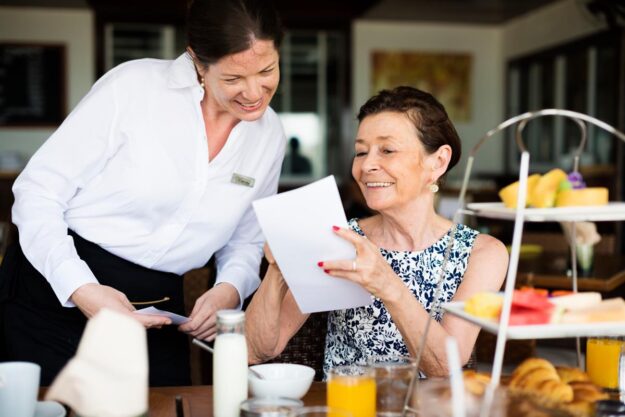 Dining Services For Seniors Senior looks at menu, surrounded by breakfast as she enjoys dining services for seniors